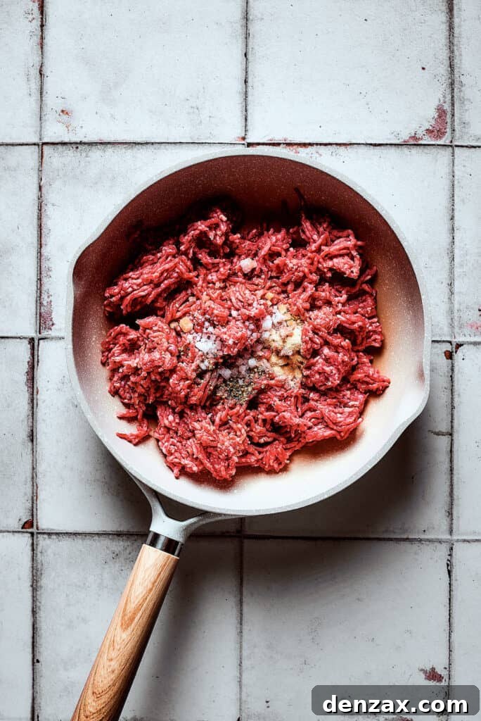 Ground beef and seasonings cooking in a skillet on the stovetop.