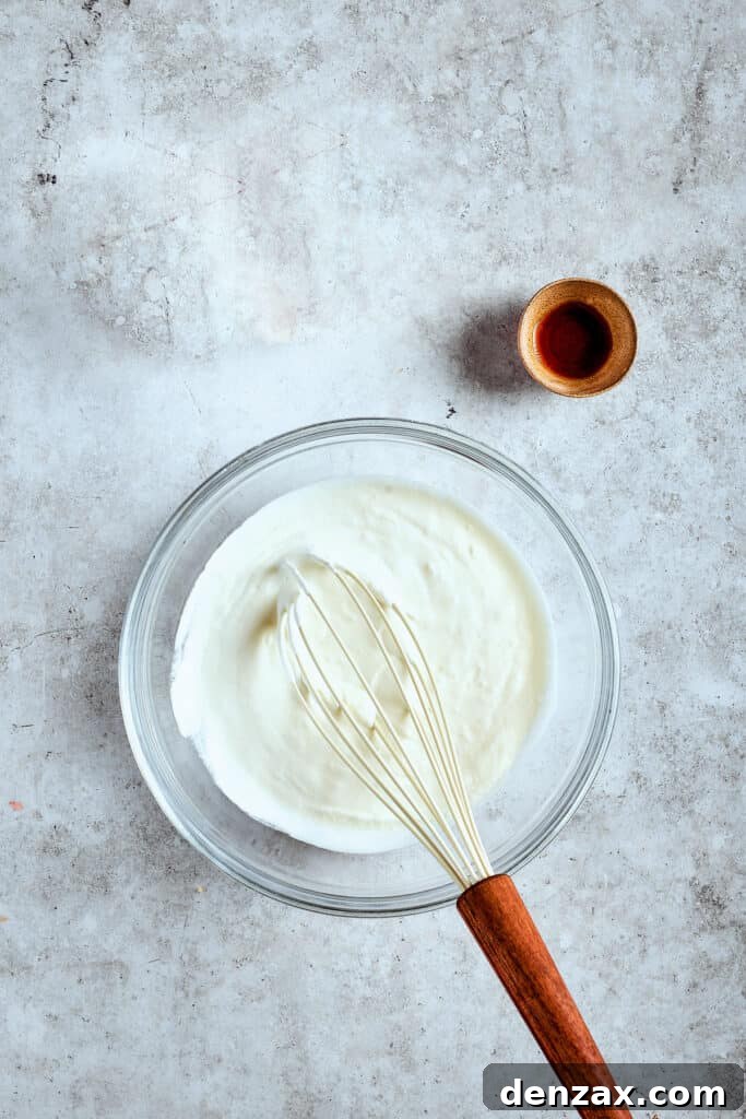 Heavy whipping cream and vanilla extract being whipped together in a mixer bowl, showing the fluffy texture starting to form.