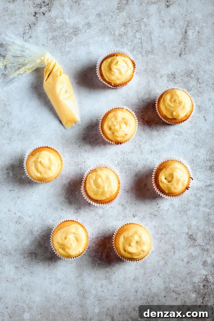 Cupcakes generously filled and topped with creamy banana pudding, ready for the final whipped cream and wafer garnishes.