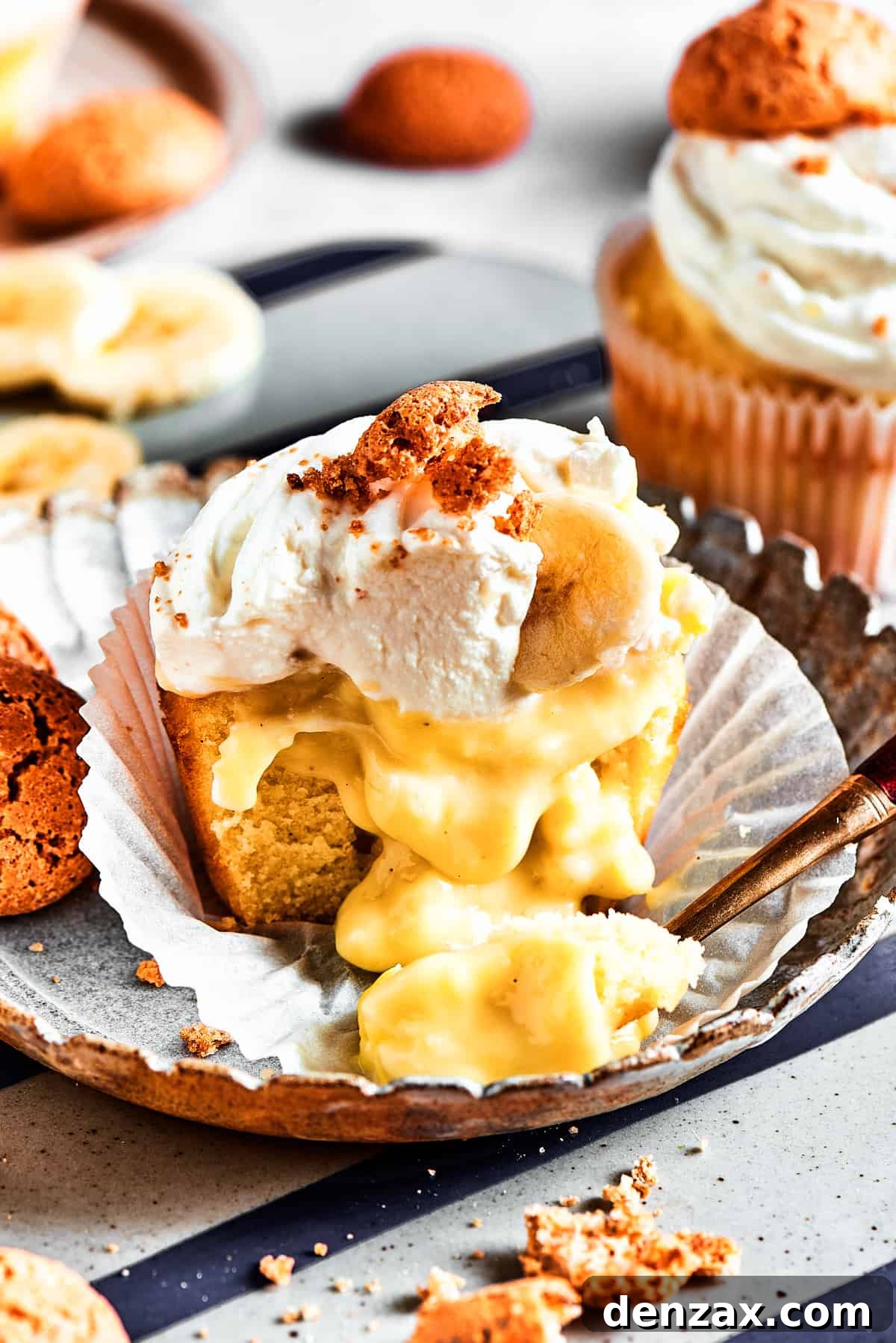 A beautifully halved banana pudding cupcake, revealing its creamy, golden banana pudding filling gently dripping out, with the wrapper peeled down.