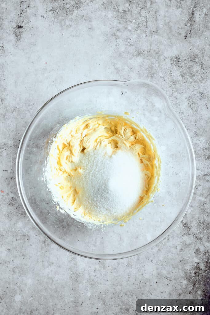 Close-up shot of softened butter and granulated sugar being creamed together in a mixing bowl with a hand mixer.
