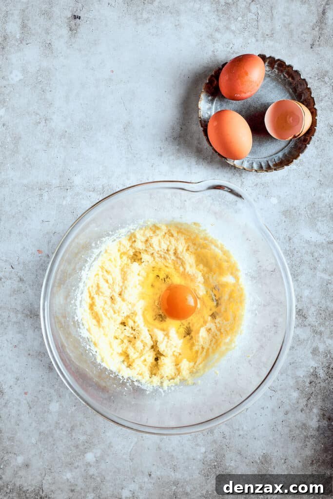 A cracked egg being added to the creamed butter and sugar mixture in a mixing bowl, illustrating the process of incorporating ingredients.