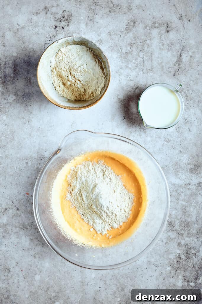 The process of adding dry ingredients to the cupcake batter in a large mixing bowl, showing the alternating steps of mixing.