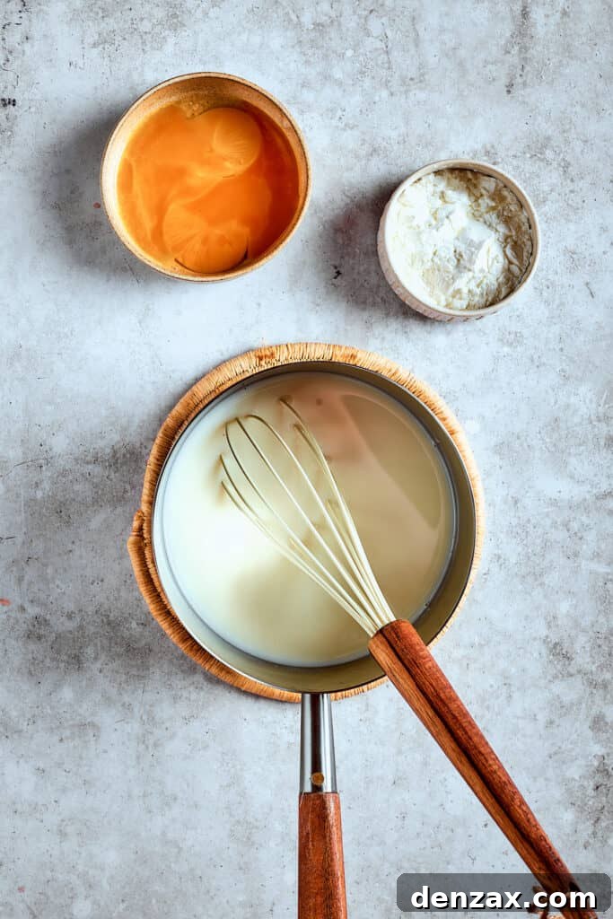 A close-up of milk and sugar being whisked together in a saucepan over medium heat, demonstrating the initial step of pudding preparation.