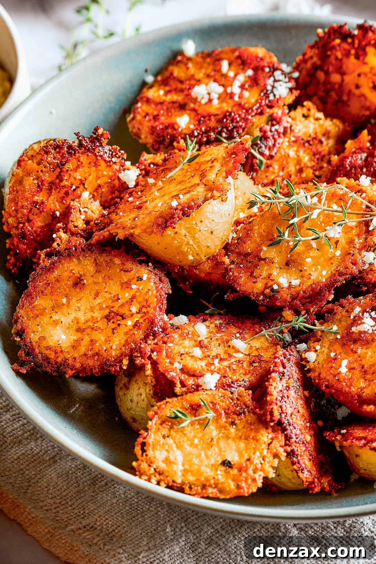 A serving of cheesy roasted potatoes in a bowl, accompanied by small cups of various dipping sauces and a clean plate.