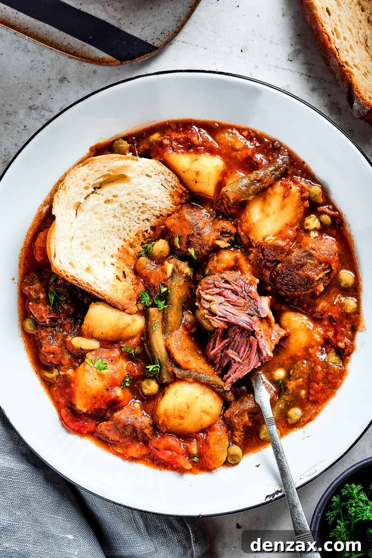 Close-up shot of a bowl of stew with a spoon, showing a piece of beef being pulled apart to reveal its tender texture.