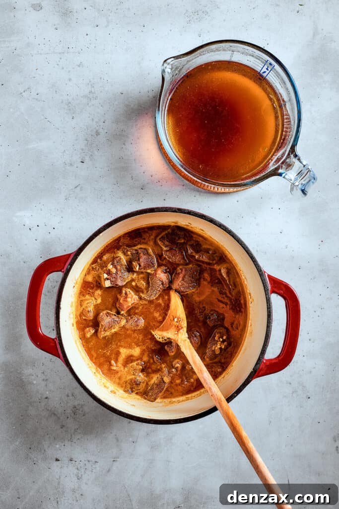 Pouring rich beef broth over browned beef chunks in a soup pot.