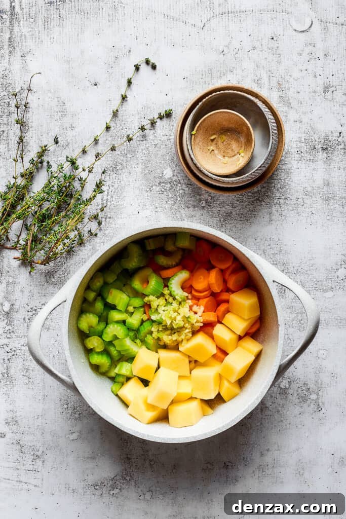 A pot filled with potatoes, celery, carrots, and onion, next to some empty bowls and thyme sprigs