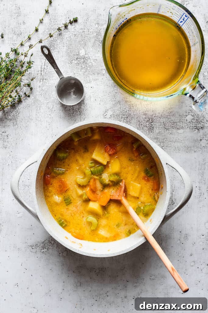 A thick veggie soup in a pot with a wooden spoon, next to a pyrex of chicken broth