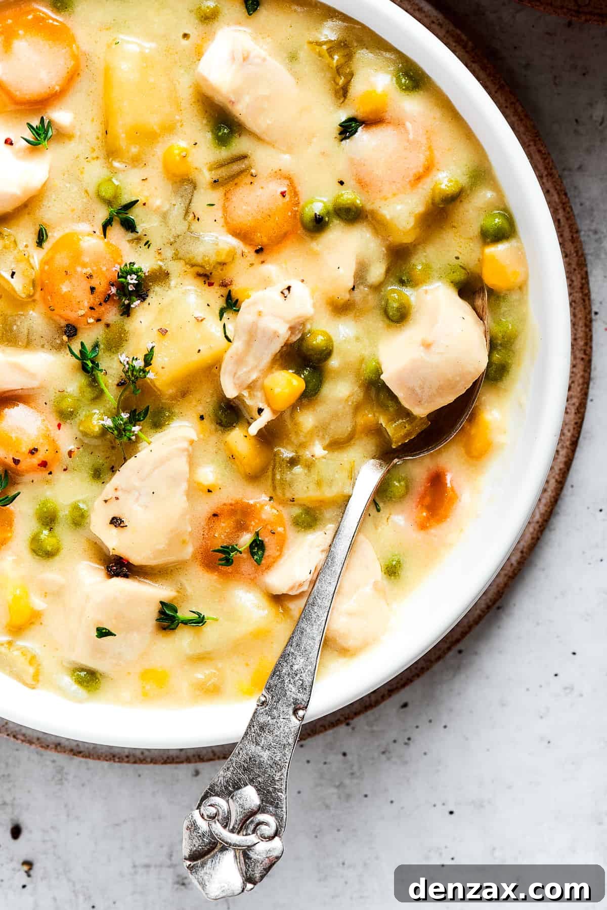 Close-up image of a bowl with chicken pot pie soup, topped with thyme, with a spoon resting in the bowl.