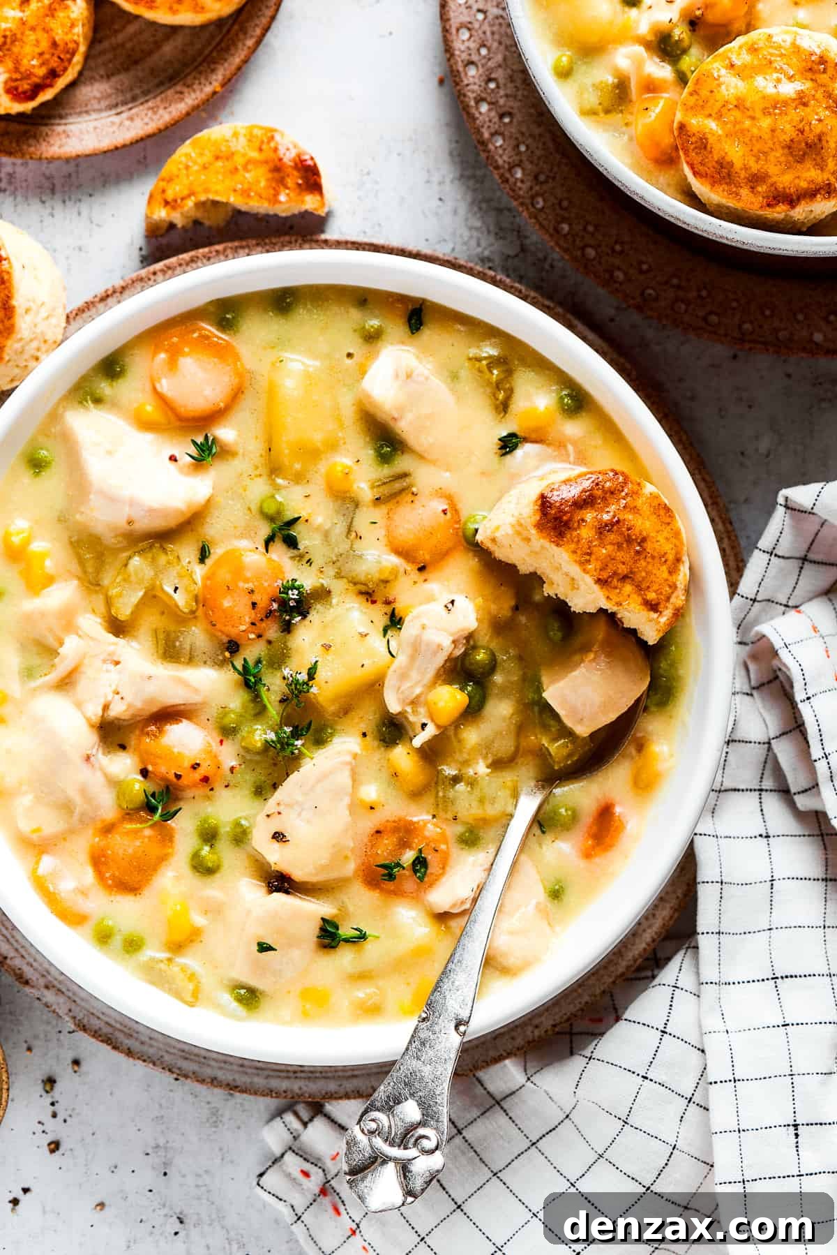 Overhead view of a bowl of chicken pot pie soup garnished with thyme, next to some biscuits.