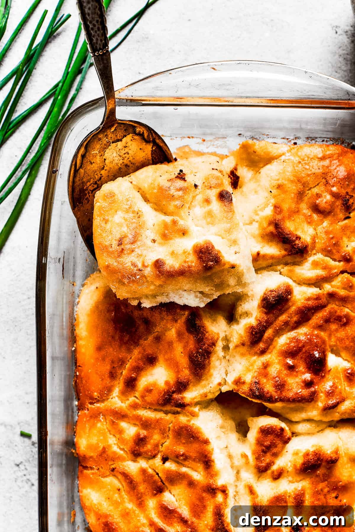 A serving spoon removing a corner piece from a pan of golden-brown butter swim biscuits, showcasing their rich, creamy texture.