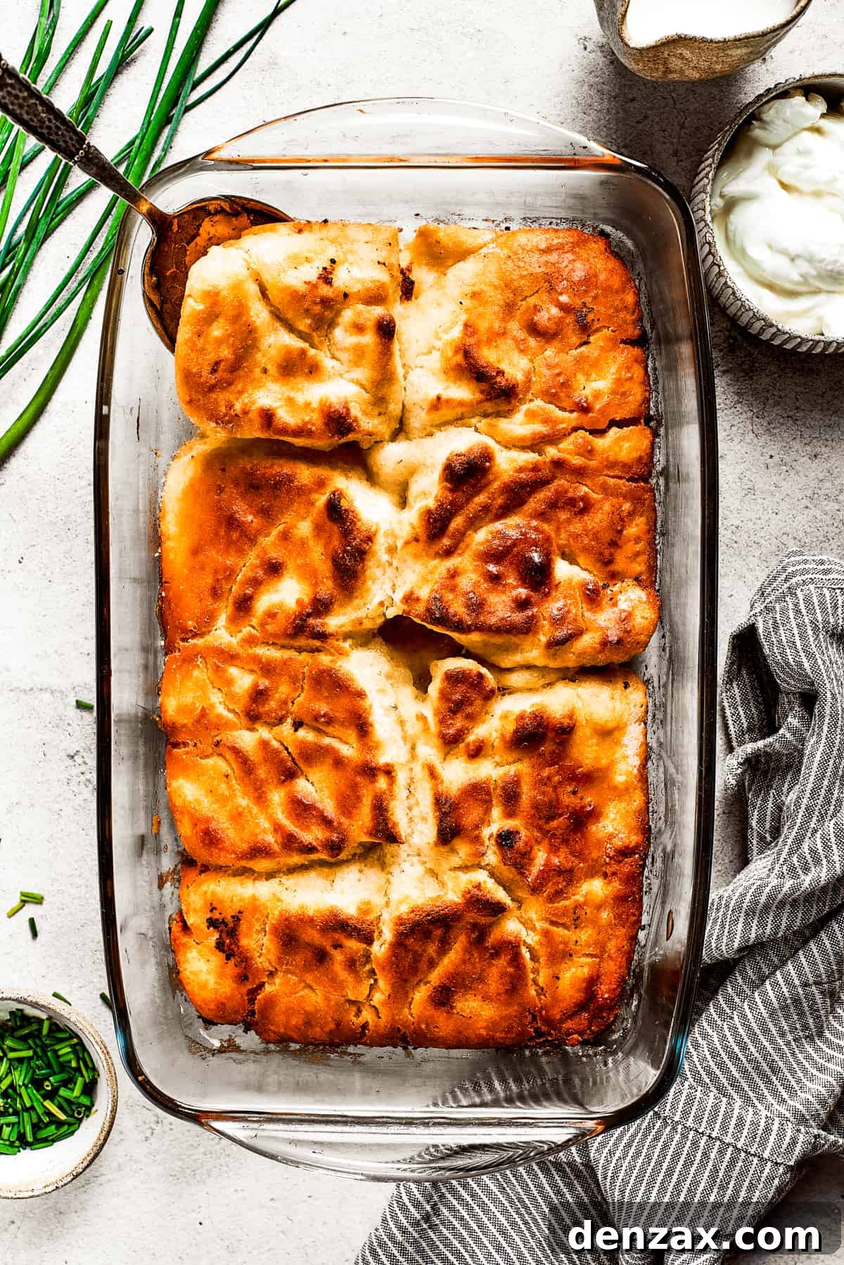 Overhead view of a baking dish filled with golden-brown butter swim biscuits, with a serving spoon gently lifting a corner piece.