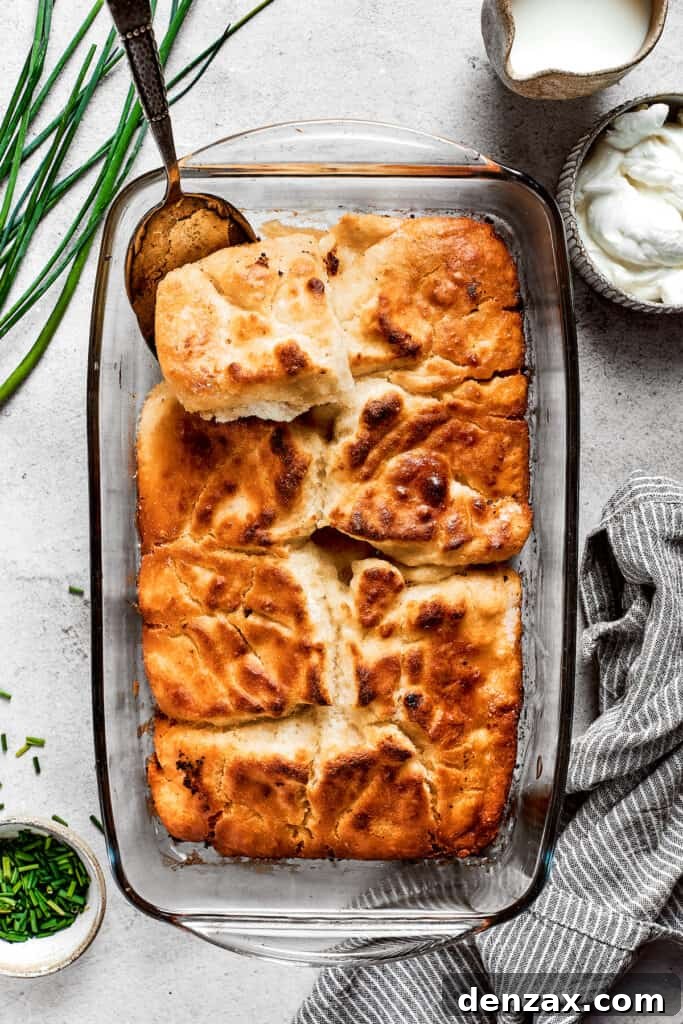 Overhead view of a baking dish filled with freshly baked, golden-brown butter swim biscuits, with a serving spoon removing a corner piece.