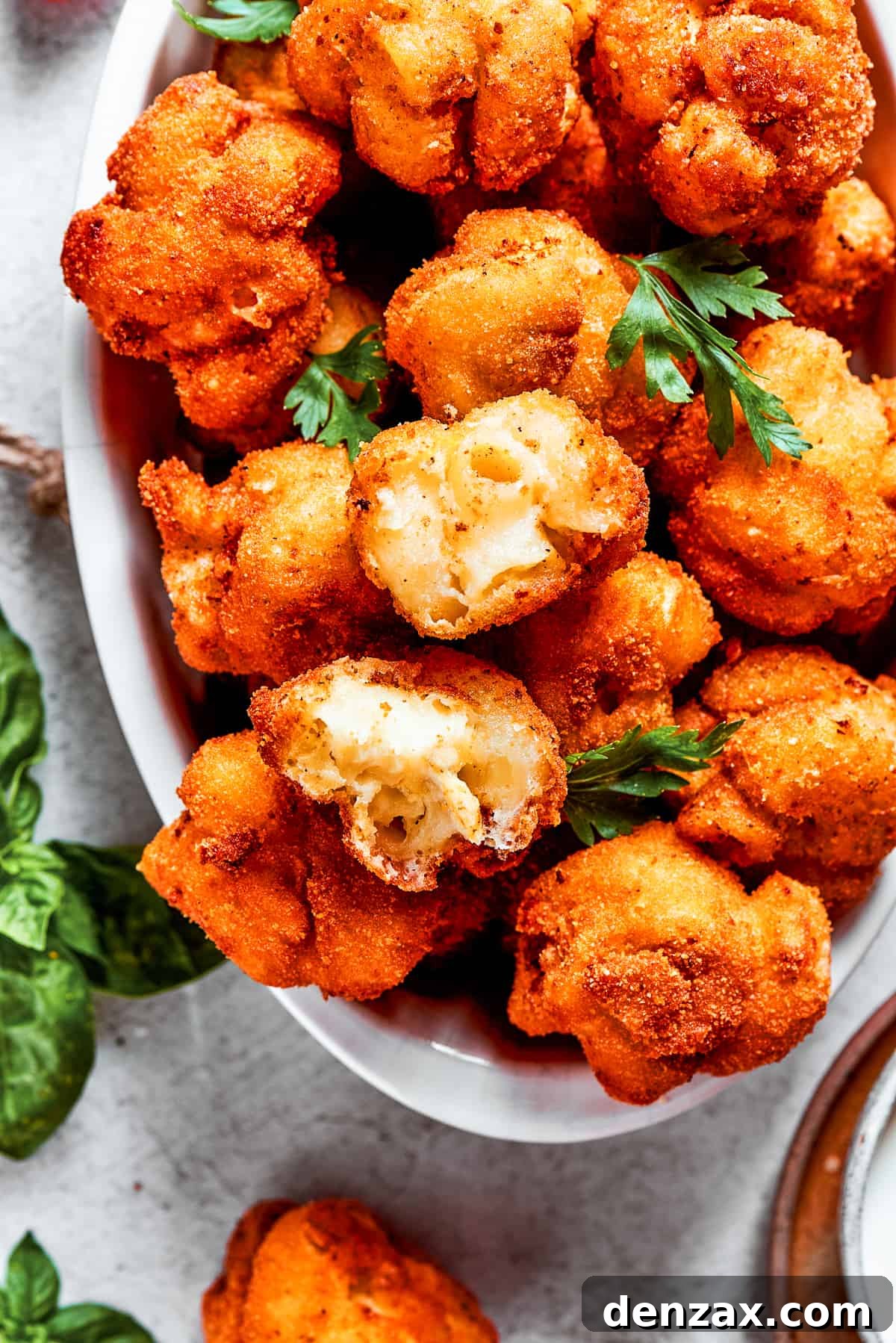 Overhead view of a beautiful plate of freshly fried mac and cheese bites, with one bite artfully pulled apart to reveal its incredibly gooey and melted cheese interior.