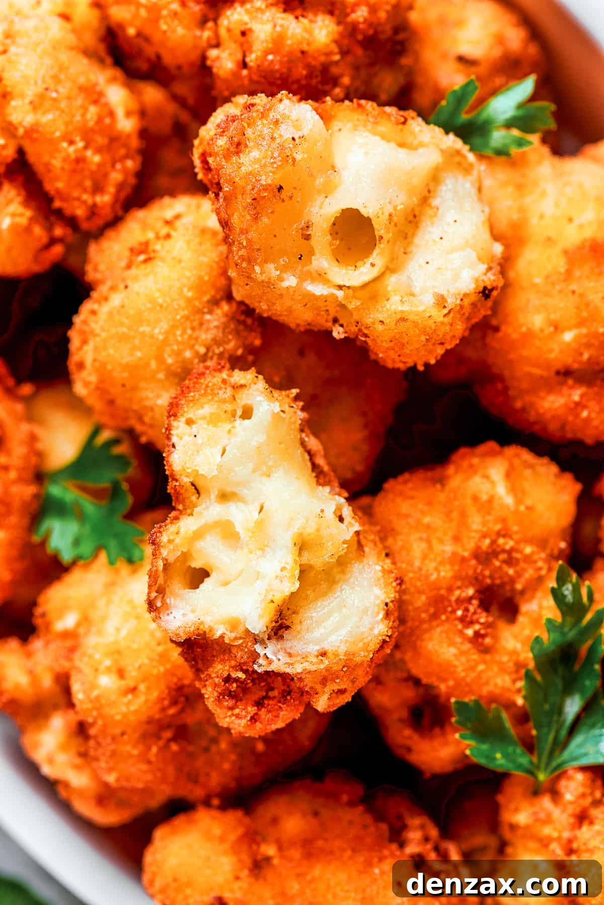 Close-up image of two perfectly fried mac and cheese bites, one cut in half to beautifully showcase its incredibly gooey, melted cheese texture inside and the golden, crispy exterior.