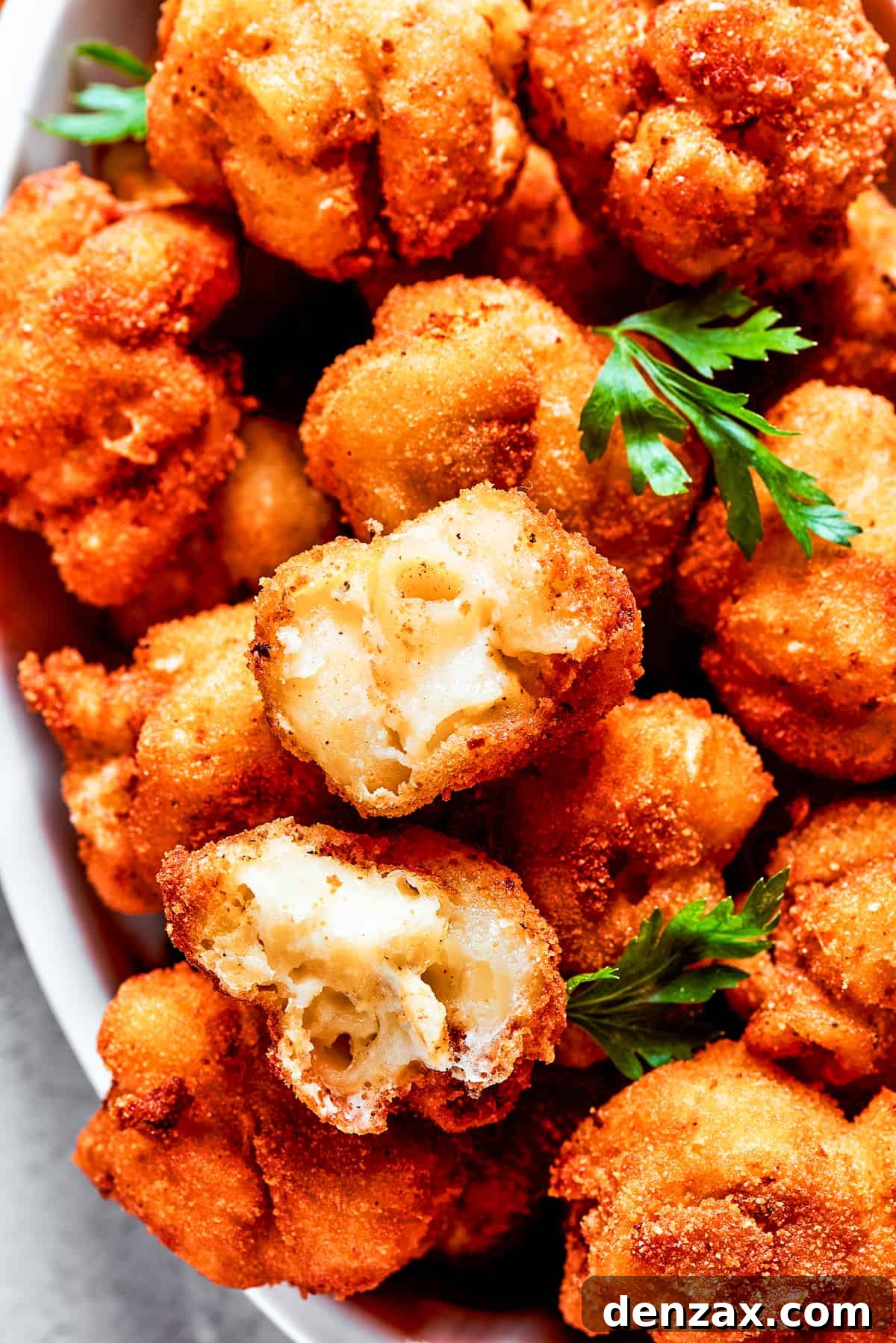 Overhead view of a beautifully arranged serving bowl filled with golden mac and cheese bites, freshly garnished with vibrant green herbs.