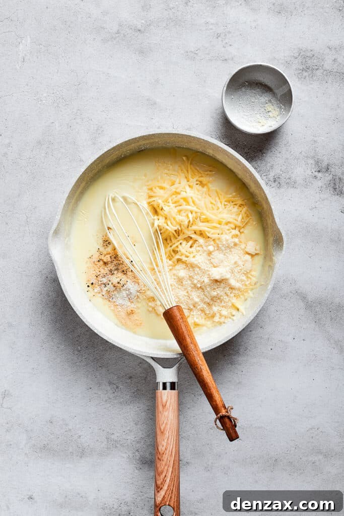 A saucepan with a whisk, showcasing shredded cheese melting beautifully into a creamy milk base.