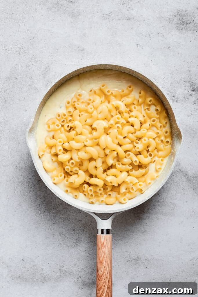 A saucepan filled with cooked macaroni pasta gracefully sitting on top of a rich and creamy cheese sauce, ready to be mixed.