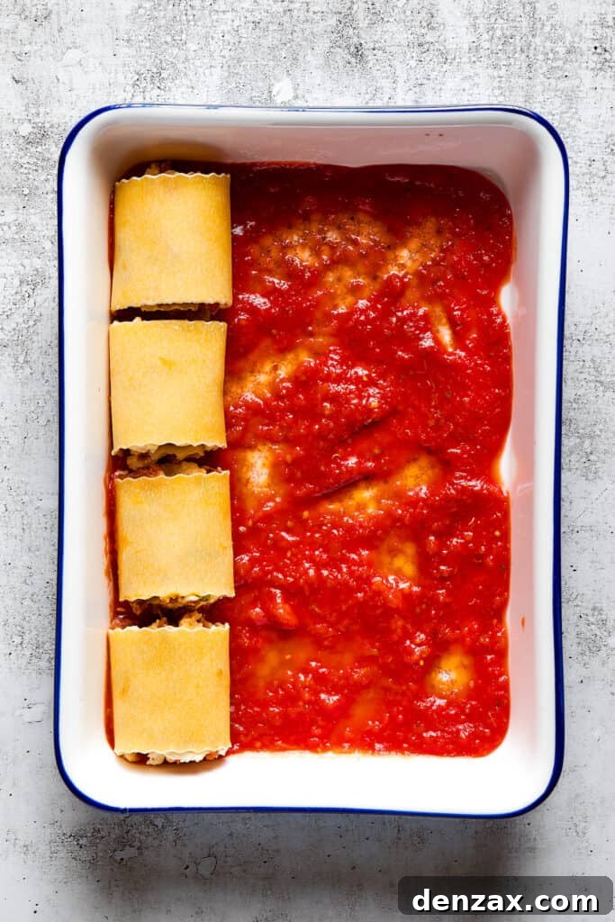 Lasagna Spirals 3 Overhead view of a baking dish partially filled with unbaked lasagna roll ups on top of marinara sauce.