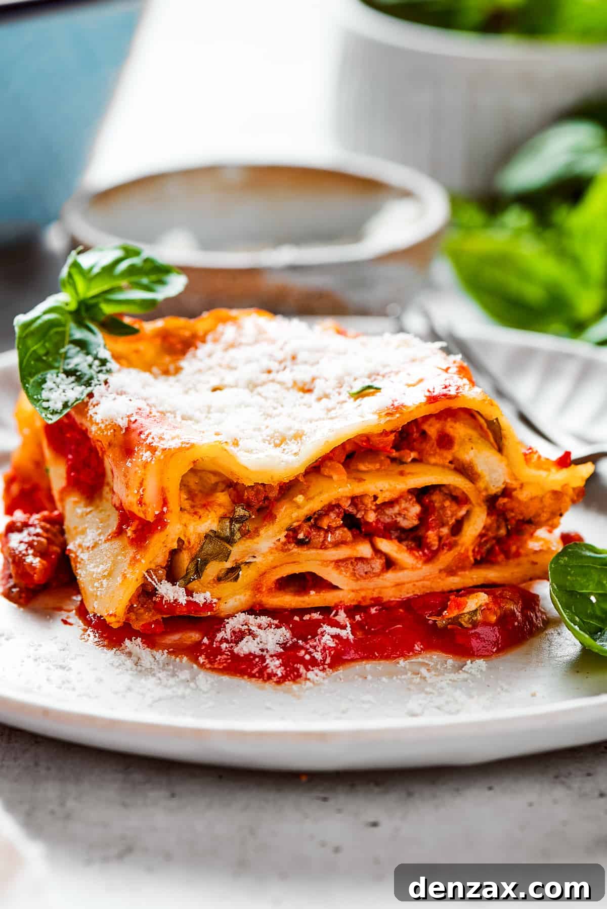 Easy lasagna roll ups have a beefy and herbaceous tomato sauce, a creamy cheese filling, tender pasta, and tons of melted cheese. Lasagna roll up served on a white dinner plate and garnished with fresh basil leaves.