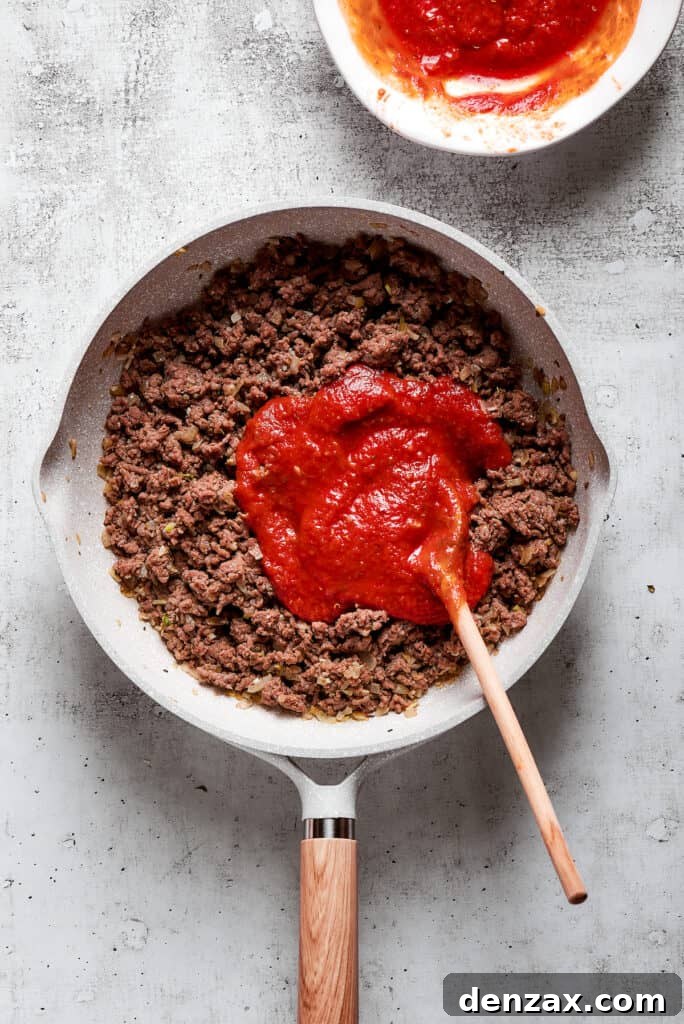 Lasagna Spirals 2 Overhead view of marinara sauce on top of cooked ground beef in a skillet with a wooden spoon.
