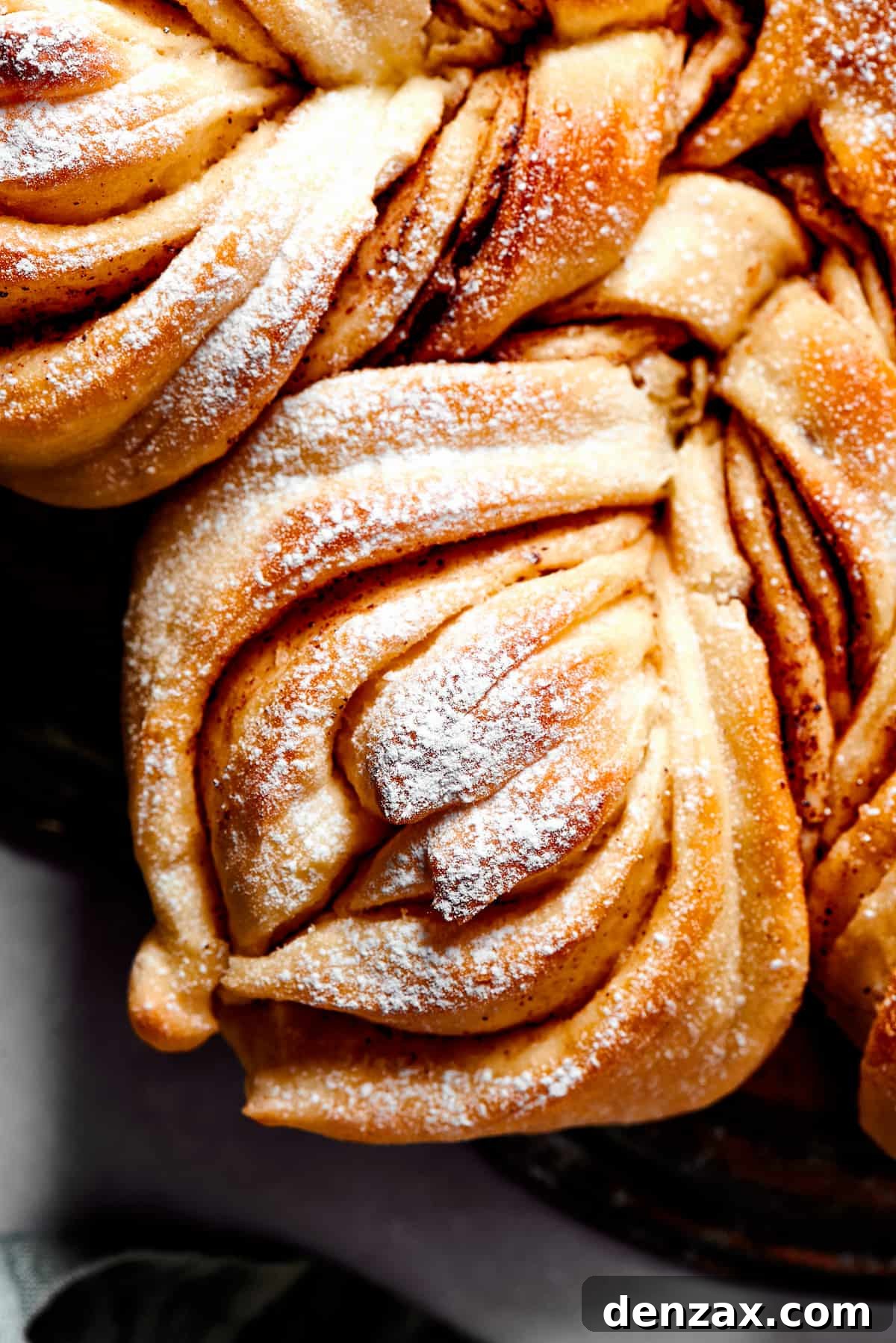 Close-up overhead view of a single, twisted segment of Star Bread, topped with a delicate dusting of powdered sugar, showcasing its tender layers and filling.