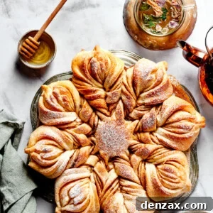 Overhead view of a star bread topped with powdered sugar, next to a bowl of honey.