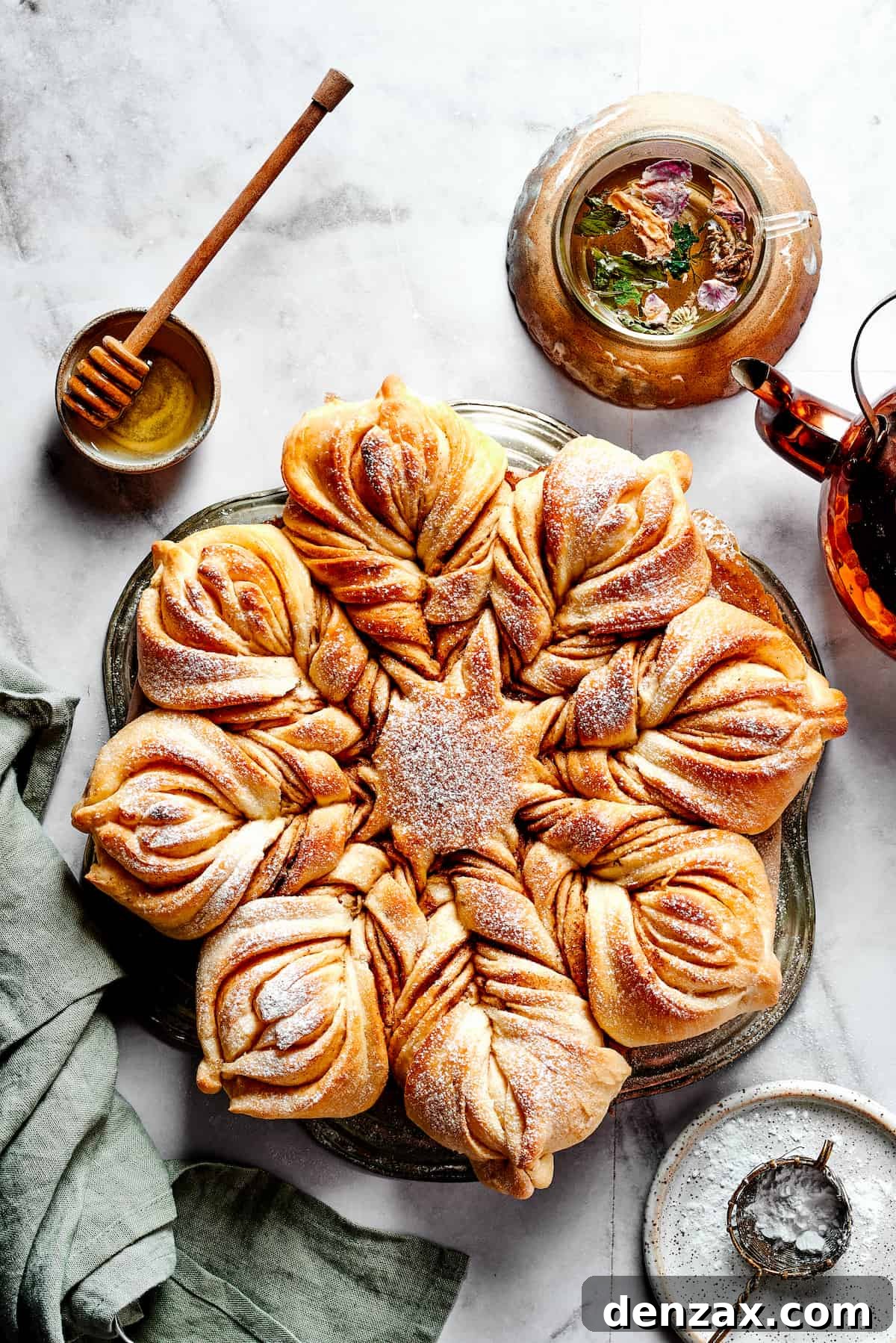 Overhead view of the freshly baked Star Bread, generously topped with powdered sugar, next to a small bowl of honey for serving.