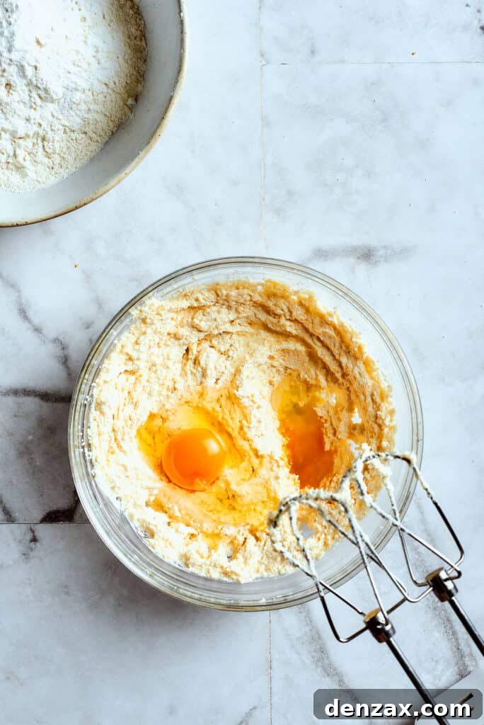 Overhead view of a mixing bowl with creamed butter and two eggs on top, ready to be mixed, demonstrating an early step in the cookie-making process.