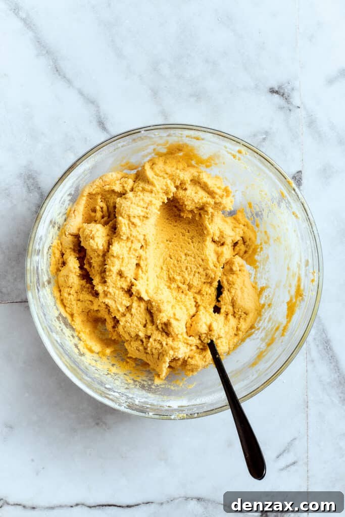 Overhead view of a mixing bowl filled with vibrant yellow lemon cookie dough, ready for chilling, with a spoon resting beside it.