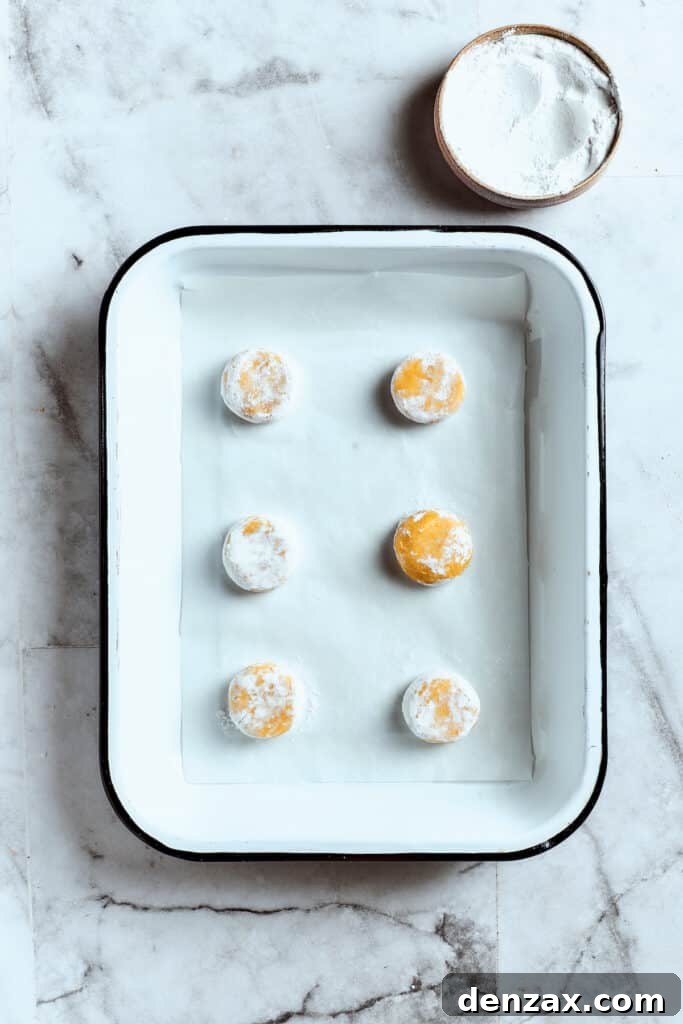 Overhead view of 6 balls of lemon cookie dough, perfectly covered in powdered sugar, nestled in a baking tray ready for the oven.