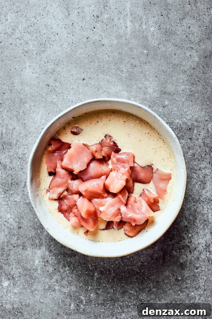 Chicken pieces in a bowl of batter.