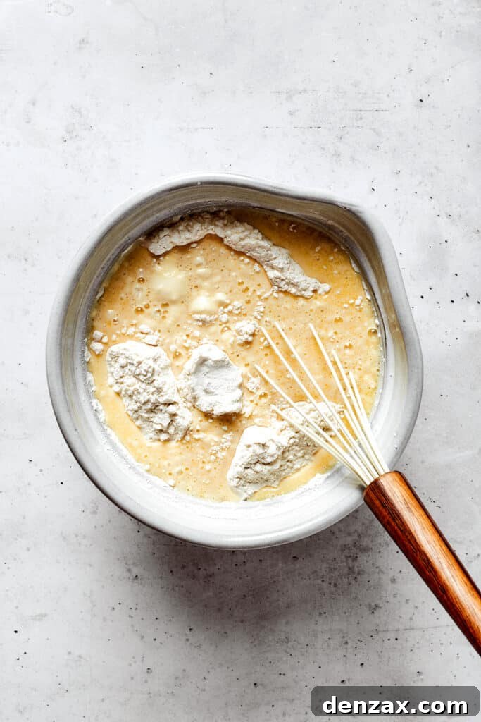 Overhead view of a mixing bowl with wet ingredients, flour, and a whisk.