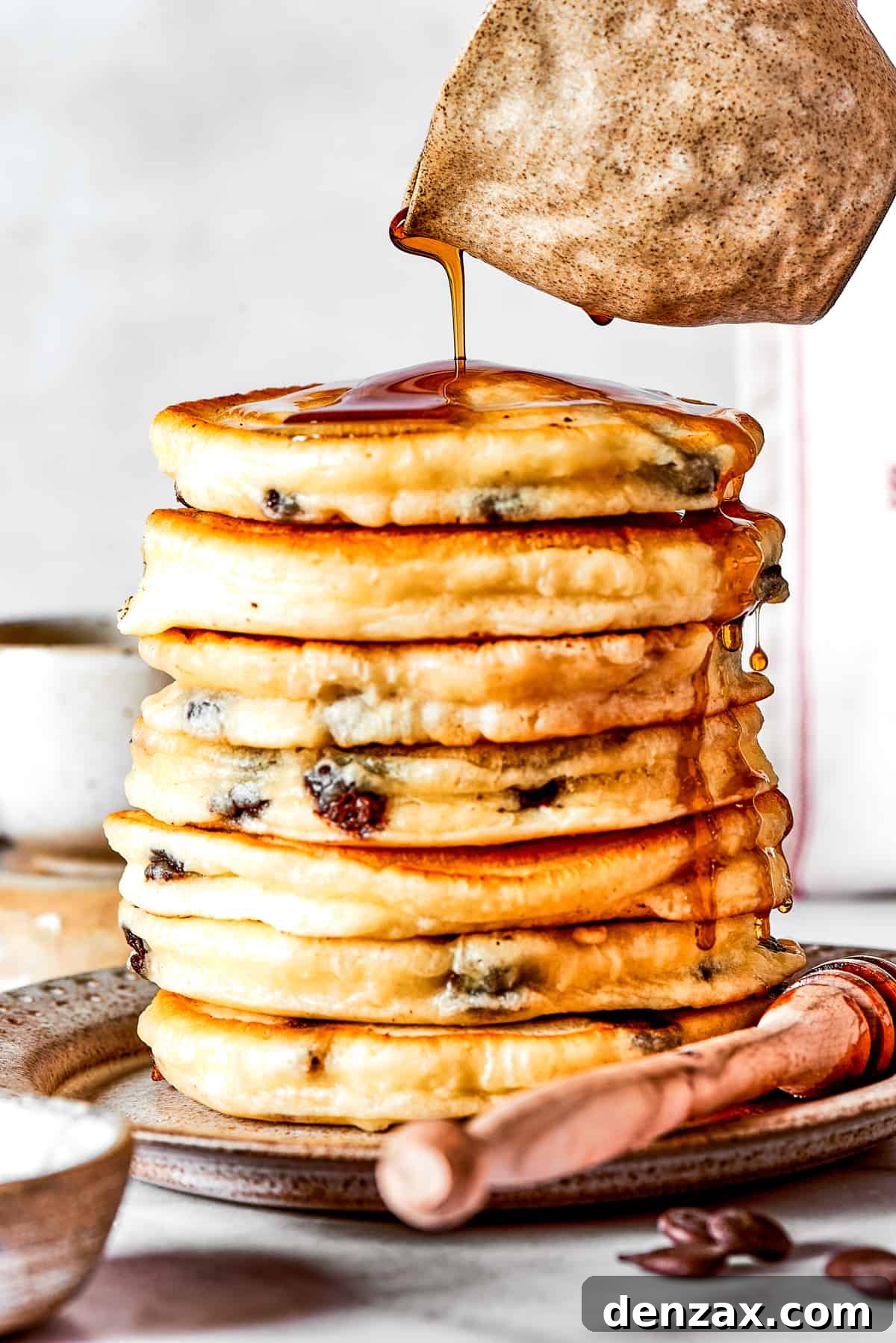 Pouring maple syrup over a stack of chocolate chip pancakes.