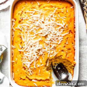 A white baking pan of baked corn souffle with a piece cut out and a spoon in the lower right side.