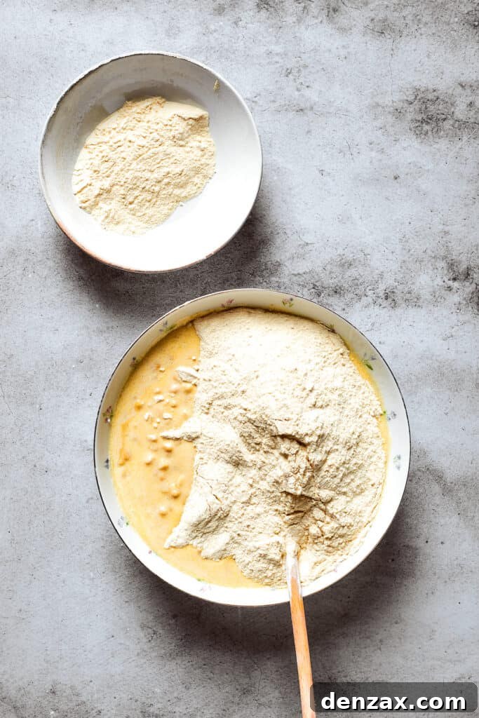 Cornbread mix is being poured into a bowl containing the corn souffle base, ready to be combined.