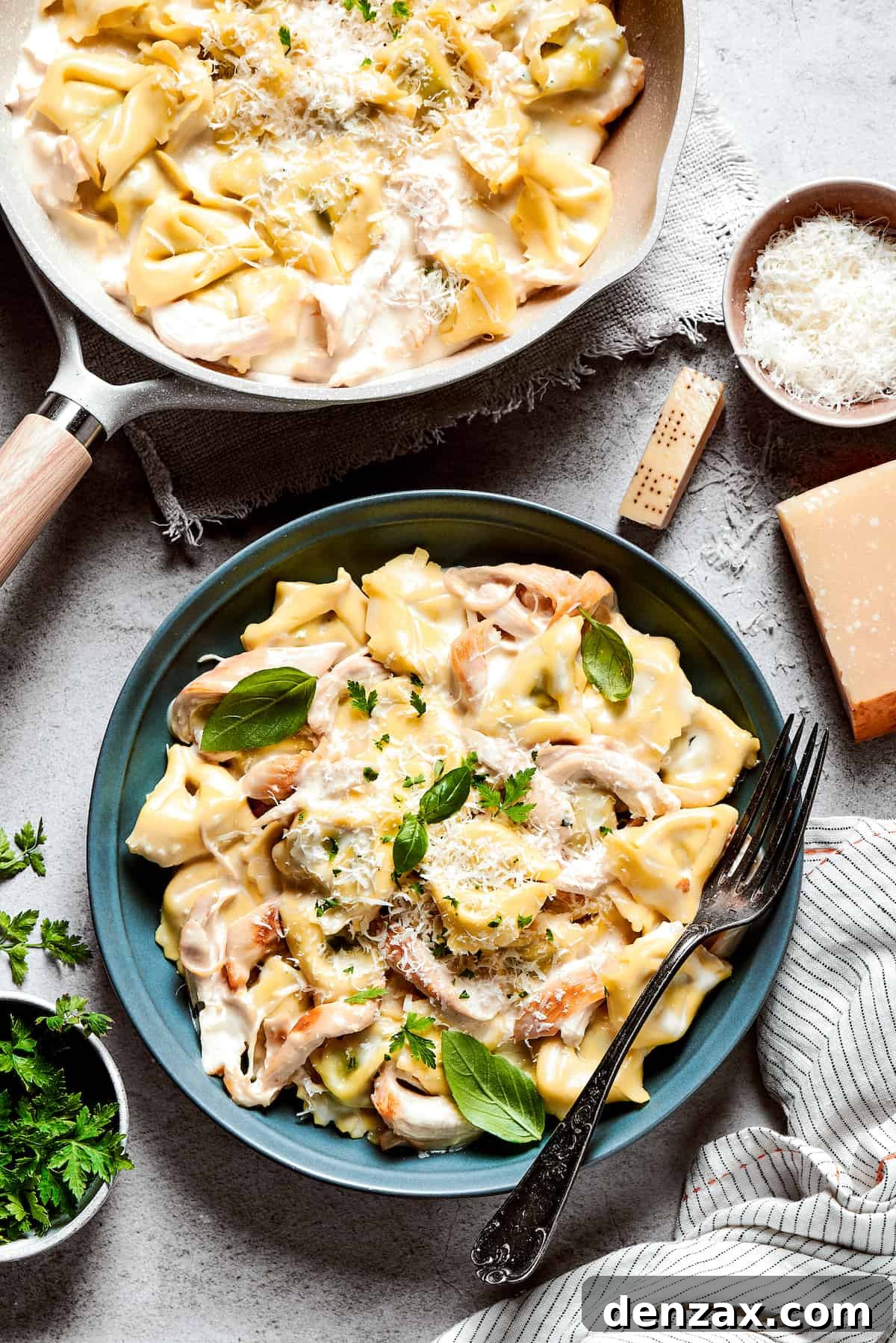 A tantalizing blue bowl of creamy Chicken Tortellini Alfredo, with a fork resting invitingly on the rim, showcasing the luscious sauce and tender pasta, positioned next to a larger skillet filled with the delicious dish, emphasizing its comforting appeal.