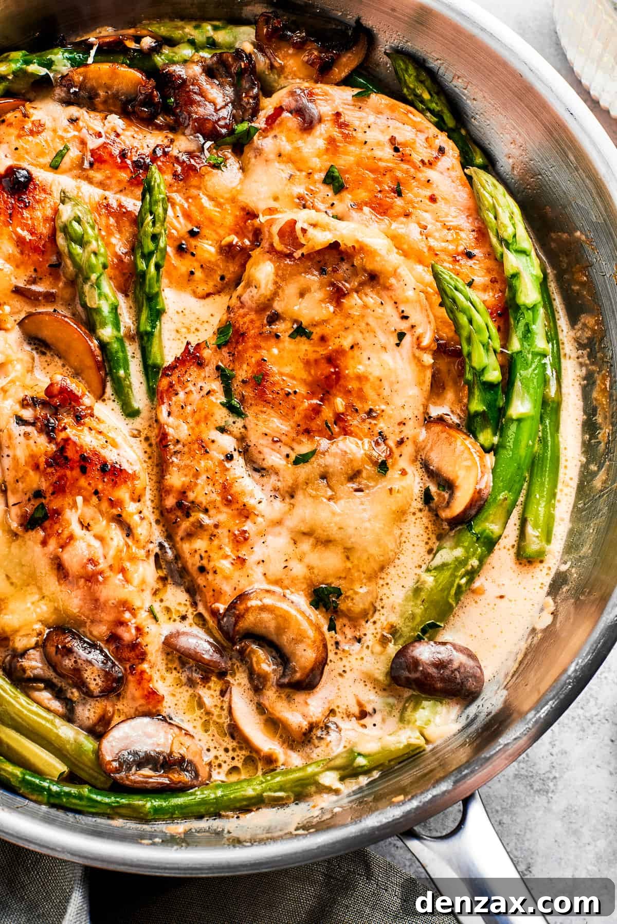 Close-up photo of chicken Madeira and asparagus spears cooking in a skillet, showcasing the rich sauce and perfectly melted cheese.