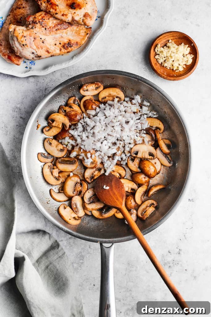 Freshly minced garlic is added to a skillet of perfectly cooked mushrooms with a wooden spoon, infusing the dish with aroma.