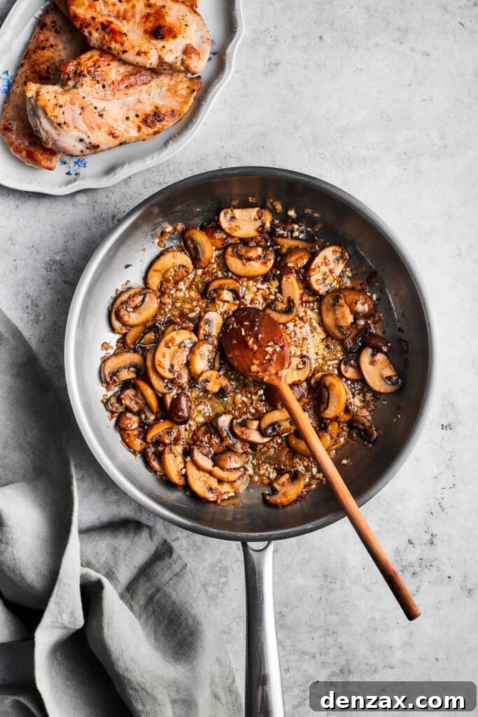 A wooden spoon gently stirs a metal skillet filled with cooked sliced mushrooms, ready for the next step in the sauce creation.