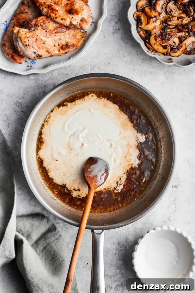 A wooden spoon stirs in rich heavy cream into the simmering sauce for chicken madeira, creating a luxurious base.