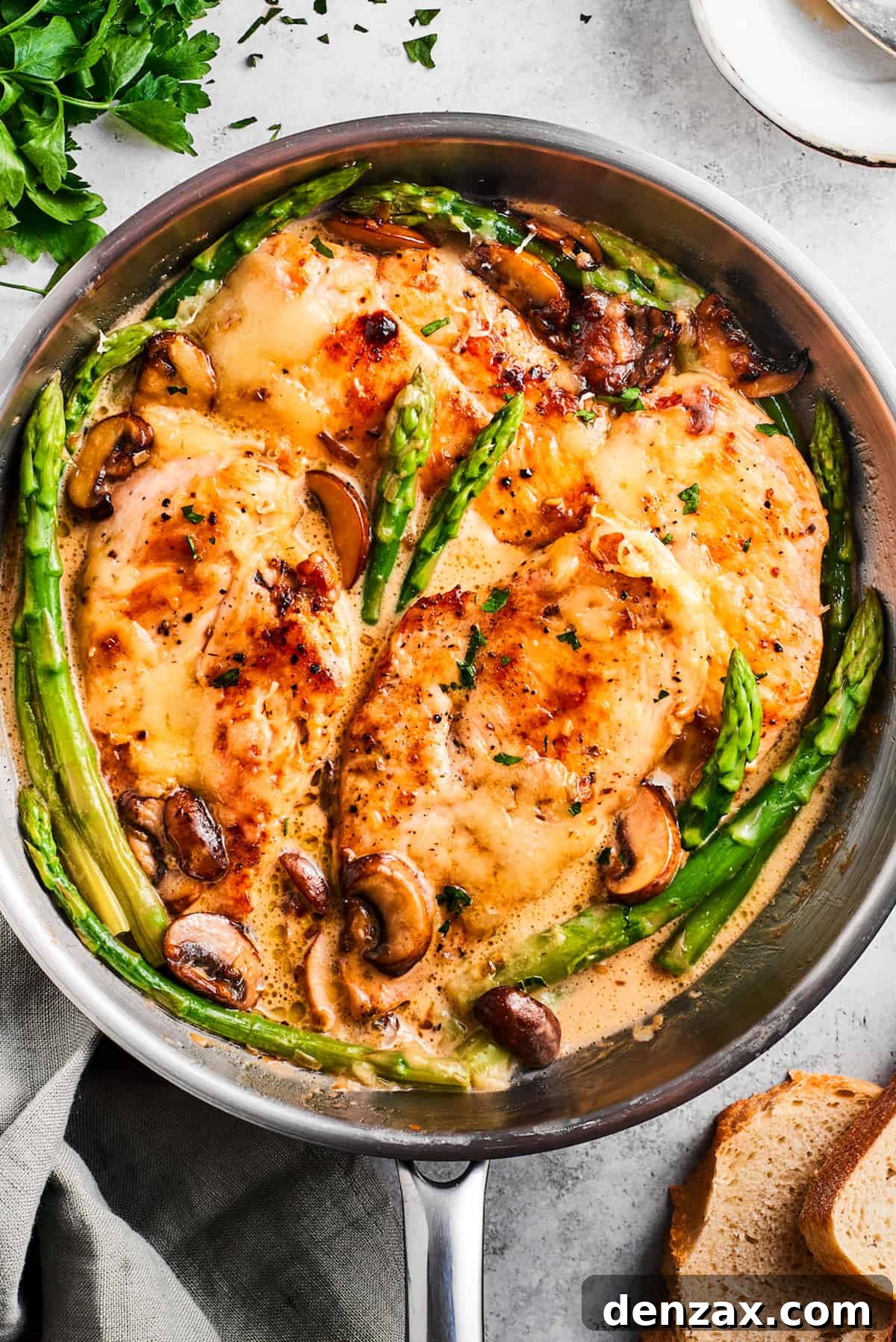 Overhead image of Chicken Madeira nestled in a skillet, beautifully garnished with asparagus spears and mushrooms, showcasing the rich, melted cheese topping.