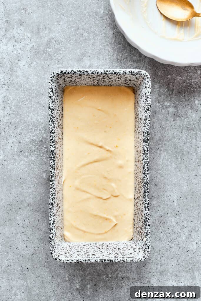 Orange cake batter is smoothed into a metal loaf pan.