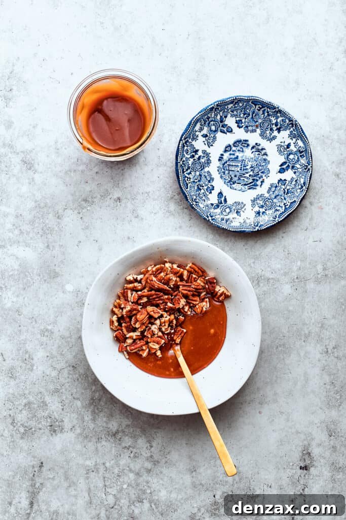 Pecans and caramel sauce are stirred together with a wooden spoon in a white bowl, preparing the middle layer for the turtle cheesecake.