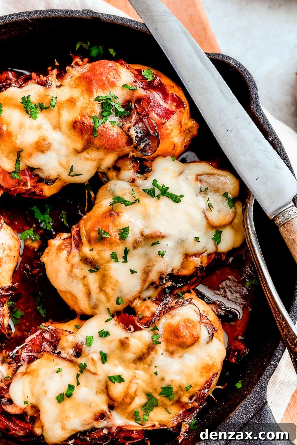 A skillet shows three chicken breasts topped with melted cheese, bacon, and mushrooms, ready to be served as Alice Springs chicken.
