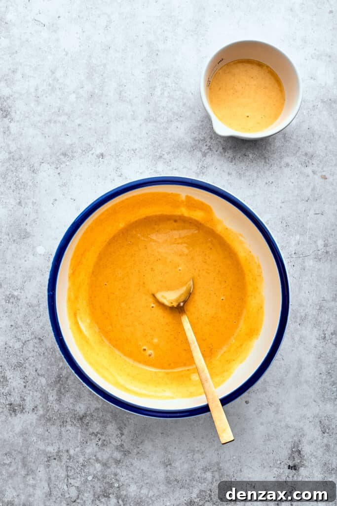 A wooden spoon combines a bright honey mustard marinade in a bowl, showcasing its smooth, creamy texture.