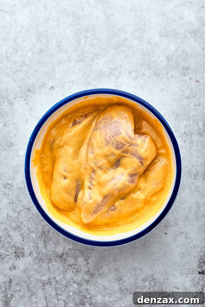 Chicken breasts marinate in a white bowl of yellow honey mustard sauce, soaking up the vibrant flavors.