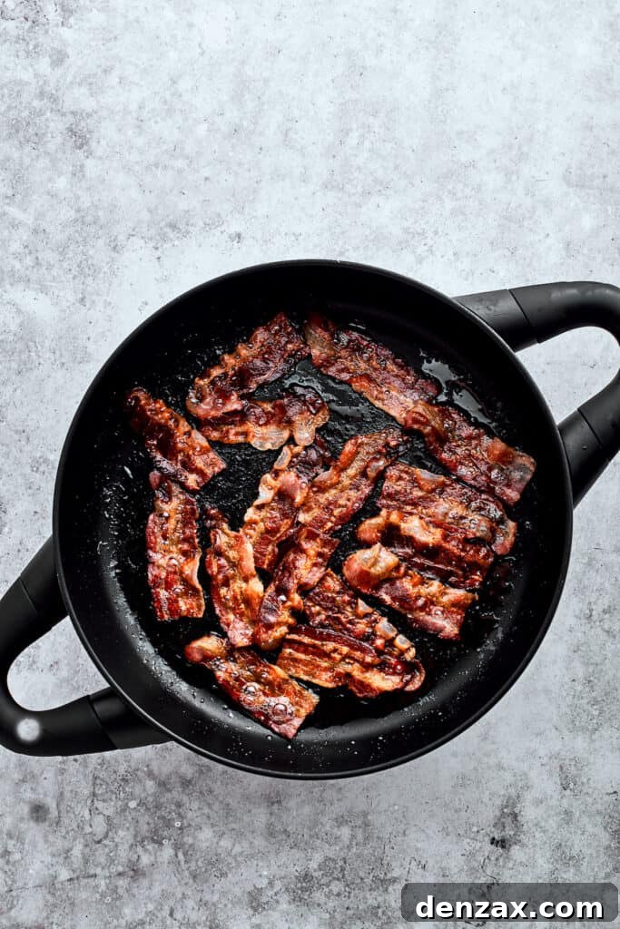 Browning bacon slices in a cast iron pot, rendering them perfectly crispy and flavorful.