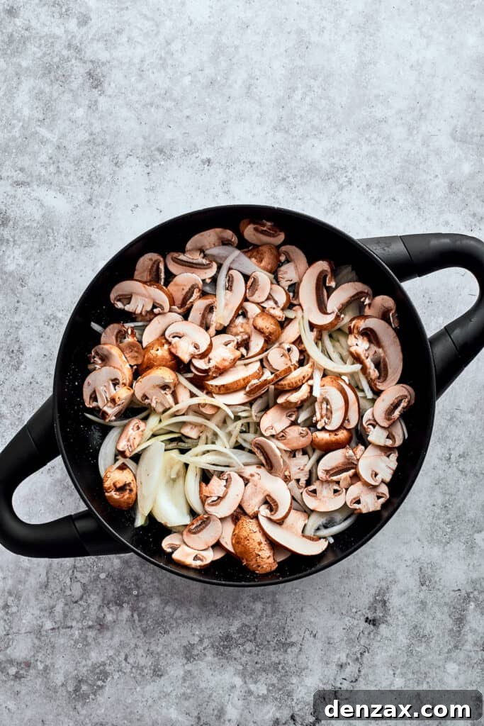 Garlic, onion, and sliced mushrooms are added to a cast iron pot, beginning to soften and caramelize.
